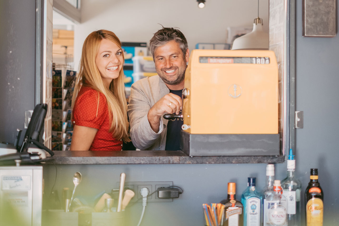 Lächelndes Gastronomenpaar an einer orangefarbenen Registrierkasse hinter dem Tresen ihres Betriebs